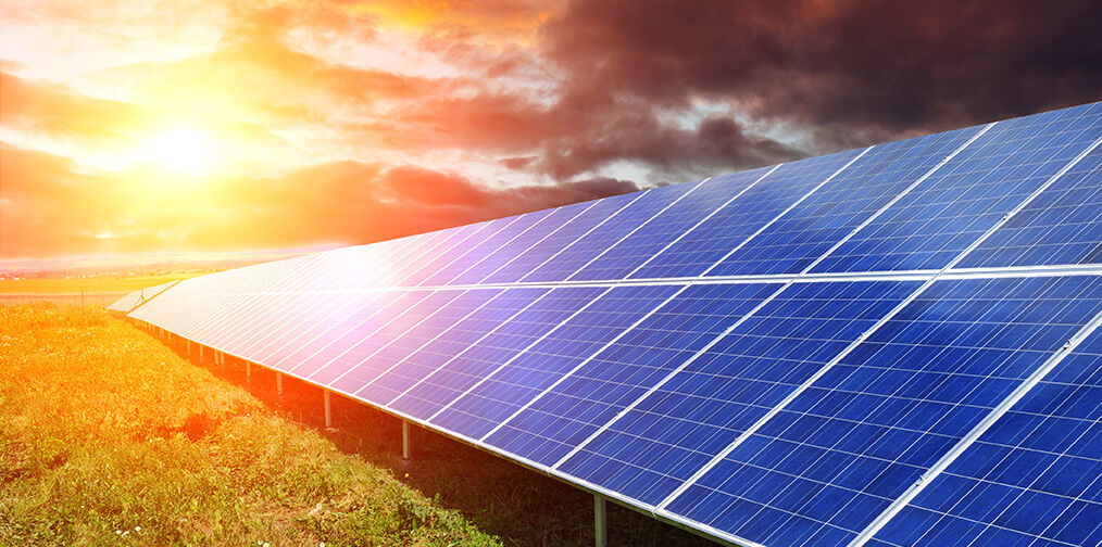 Eine Reihe von Solarpaneelen steht auf einem grünen Feld, während die Sonne am Horizont untergeht und den Himmel in warmen Farben erstrahlen lässt. Eine Reihe von Solarpaneelen steht auf einem grünen Feld, während die Sonne am Horizont untergeht und den Himmel in warmen Farben erstrahlen lässt.