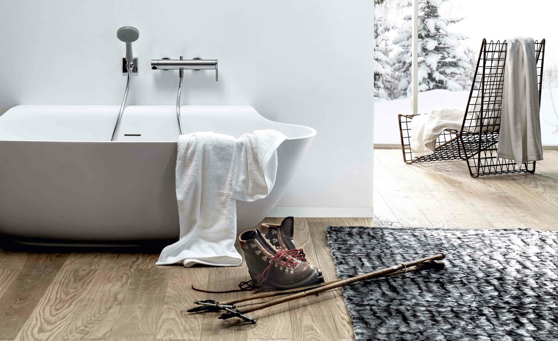 Ein schlichtes Badezimmer mit freistehender Wanne, weißen Wänden und Holzboden. Ein Fenster zeigt eine verschneite Landschaft, Ski und Stiefel stehen bereit. Ein schlichtes Badezimmer mit freistehender Wanne, weißen Wänden und Holzboden. Ein Fenster zeigt eine verschneite Landschaft, Ski und Stiefel stehen bereit.