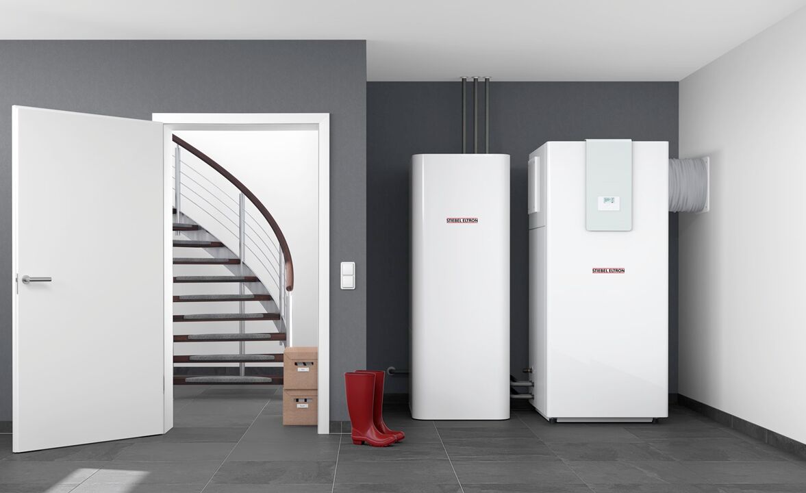Ein heller Heizraum mit weißen Geräten von Stiebel Eltron und sauberer Anordnung. Daneben stehen rote Gummistiefel und ein geöffneter Zugang zu einer Treppe. Luft Wasser Wärmepumpe Innenaufstellung