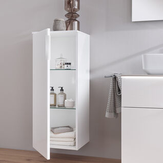 Ein eleganter, weißer Hängeschrank mit Glaseinlegeböden im Bad, gefüllt mit Handtüchern und Pflegeprodukten, daneben ein Waschbecken und Handtücher.