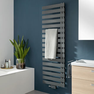 Moderner, grauer Handtuchheizkörper an dunkelblauer Wand, mit Handtuch. Daneben Pflanzen und ein Waschbecken mit Holzschrank. Stilvolles Badezimmerdesign. Moderner, grauer Handtuchheizkörper an dunkelblauer Wand, mit Handtuch. Daneben Pflanzen und ein Waschbecken mit Holzschrank. Stilvolles Badezimmerdesign.