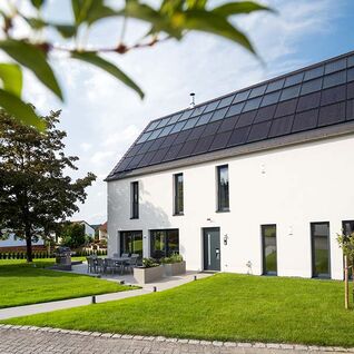 Ein modernes Haus mit Solarpaneelen auf dem Dach, umgeben von einem gepflegten Garten, unter klarem, blauem Himmel.