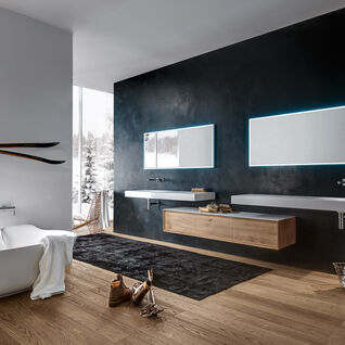 Badezimmer mit freistehender Badewanne, beleuchteten Spiegeln, Holzwaschtisch, Skiern an der Wand und großem Fenster. Elegante, gemütliche Atmosphäre. Badezimmer mit freistehender Badewanne, beleuchteten Spiegeln, Holzwaschtisch, Skiern an der Wand und großem Fenster. Elegante, gemütliche Atmosphäre.