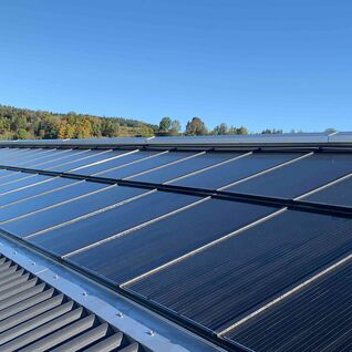 Solarpaneele auf einem geneigten Dach, umgeben von einer gr&uuml;nen Landschaft und blauem Himmel.