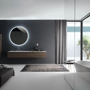 Modernes Badezimmer mit beleuchtetem, rundem Spiegel, schwebendem Waschtisch und gro&szlig;em Fenster, das viel Licht hereinl&auml;sst. Elegantes, minimalistisches Design.