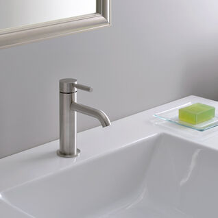 Nahaufnahme eines modernen Waschbeckens mit einfachem Wasserhahn. Auf der weißen Fläche liegt eine Seifenschale mit grüner Seife. Im Hintergrund ein Handtuch. Nahaufnahme eines modernen Waschbeckens mit einfachem Wasserhahn. Auf der weißen Fläche liegt eine Seifenschale mit grüner Seife. Im Hintergrund ein Handtuch.