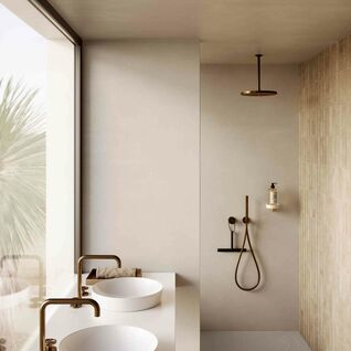 Ein lichtdurchflutetes Badezimmer mit gro&szlig;en Fenstern, zwei runden Waschbecken und goldenen Armaturen. Die begehbare Dusche hat warme, neutrale Fliesen.