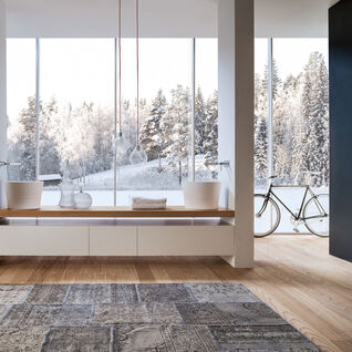 Ger&auml;umiges, modernes Badezimmer mit Holzfu&szlig;boden, freistehenden Waschbecken, gro&szlig;en Fenstern mit Blick auf verschneite Landschaft und dekorativem Teppich.