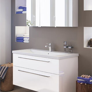 Modernes Badezimmer mit weißem Waschtisch und Spiegel mit Beleuchtung. Eingebaute Regale mit Handtüchern, schlichte Dekoration und neutrale Wandfarben. Modernes Badezimmer mit weißem Waschtisch und Spiegel mit Beleuchtung. Eingebaute Regale mit Handtüchern, schlichte Dekoration und neutrale Wandfarben.