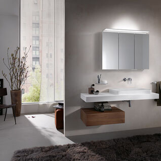 Modernes Badezimmer mit wandmontiertem Waschbecken, beleuchtetem Spiegelschrank und Holzunterschrank, ergänzt durch große Fenster und einen flauschigen Teppich. Modernes Badezimmer mit wandmontiertem Waschbecken, beleuchtetem Spiegelschrank und Holzunterschrank, ergänzt durch große Fenster und einen flauschigen Teppich.