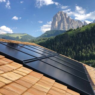 Solarpaneele auf einem Holzdach mit einer beeindruckenden Berglandschaft im Hintergrund.