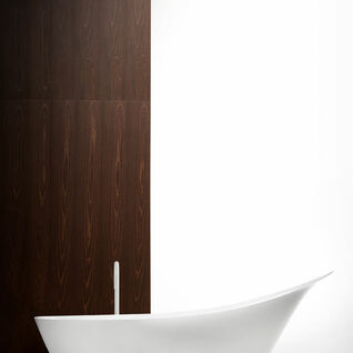 Ein modernes Badezimmer mit einer eleganten, wei&szlig;en, freistehenden Badewanne. Die Wand im Hintergrund ist aus dunklem Holz, der Raum wirkt minimalistisch.