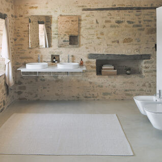 Rustikales Badezimmer mit Steinwänden, Doppelwaschbecken, modernen WC und Bidet. Integrierte Ablage, helle Fensterbeleuchtung, schwebende Ablage.