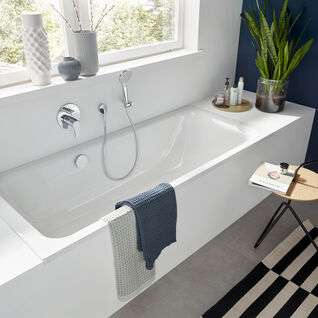 Modernes Bad mit weißer Badewanne, Pflanzen, dekorativen Vasen und gestreiftem Teppich. Viel natürliches Licht und schlichte Eleganz prägen den Raum. Modernes Bad mit weißer Badewanne, Pflanzen, dekorativen Vasen und gestreiftem Teppich. Viel natürliches Licht und schlichte Eleganz prägen den Raum.
