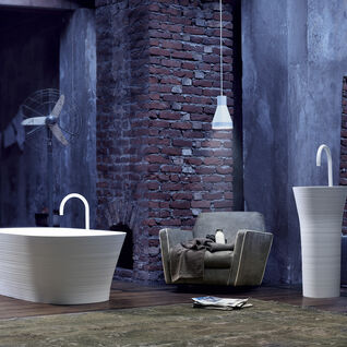 Moderne weiße Badewanne und Waschbecken vor Backsteinwand. Sessel, Ventilator und Pendelleuchte schaffen ein industrielles Ambiente. Moderne weiße Badewanne und Waschbecken vor Backsteinwand. Sessel, Ventilator und Pendelleuchte schaffen ein industrielles Ambiente.