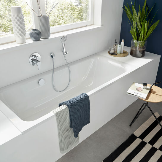 Modernes Badezimmer mit eingebauter Wanne, blauer Akzentwand, Pflanzen, gestreiftem Teppich und stilvollen Dekorationen für gemütliches Ambiente. Modernes Badezimmer mit eingebauter Wanne, blauer Akzentwand, Pflanzen, gestreiftem Teppich und stilvollen Dekorationen für gemütliches Ambiente.