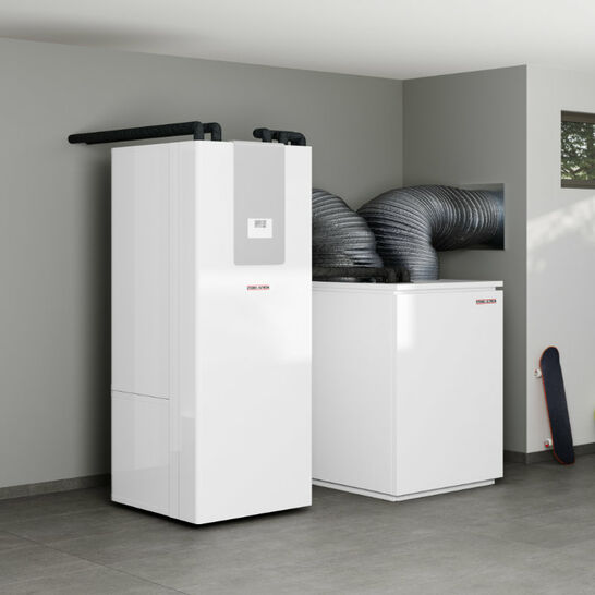 Das Bild zeigt eine moderne Heizungsanlage, möglicherweise eine Wärmepumpe, mit zwei weißen Geräten und Lüftungsrohren in einem Hauswirtschaftsraum. Inhaus Luft Wasser Wärmepumpe Innenaufstellung