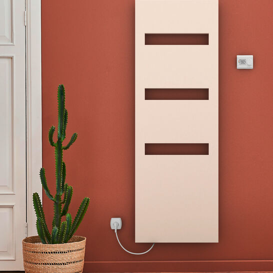 Moderner, cremefarbener Heizkörper mit rechteckigen Ausschnitten, an einer terrakottafarbenen Wand. Ein Kaktus in einem Korb verleiht dem Raum einen natürlichen Akzent. Moderner, cremefarbener Heizkörper mit rechteckigen Ausschnitten, an einer terrakottafarbenen Wand. Ein Kaktus in einem Korb verleiht dem Raum einen natürlichen Akzent.