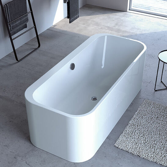 Eine freistehende, rechteckige Badewanne in einem modernen Badezimmer mit grauem Boden, Waschbecken, Handtuchhalter und Fenster. Minimalistisches Design.