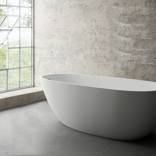 Modernes Badezimmer mit freistehender, ovaler Badewanne. Die Umgebung hat eine industrielle &Auml;sthetik mit Sichtbetonw&auml;nden und einem gro&szlig;en Fenster, das viel nat&uuml;rliches Licht hereinl&auml;sst.
