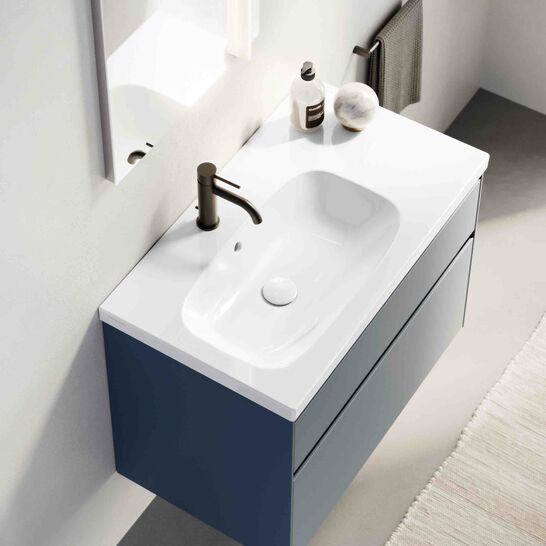 Moderner Waschtisch mit blauem, schwebendem Unterschrank und wei&szlig;er Oberfl&auml;che. Schwarzer Wasserhahn, dezente Dekoration und Handtuchhalter an der Seite.