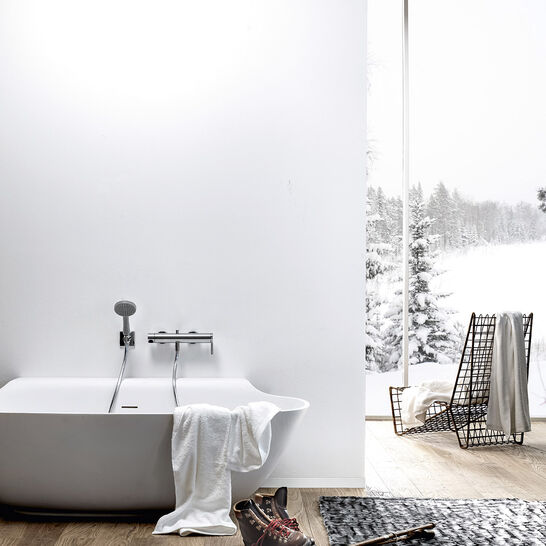 Helles Badezimmer mit freistehender Badewanne, großem Fenster mit Blick auf verschneite Landschaft, Holzfußboden und minimalistischer Dekoration. Skistock und Schuhe als Akzent. Helles Badezimmer mit freistehender Badewanne, großem Fenster mit Blick auf verschneite Landschaft, Holzfußboden und minimalistischer Dekoration. Skistock und Schuhe als Akzent.