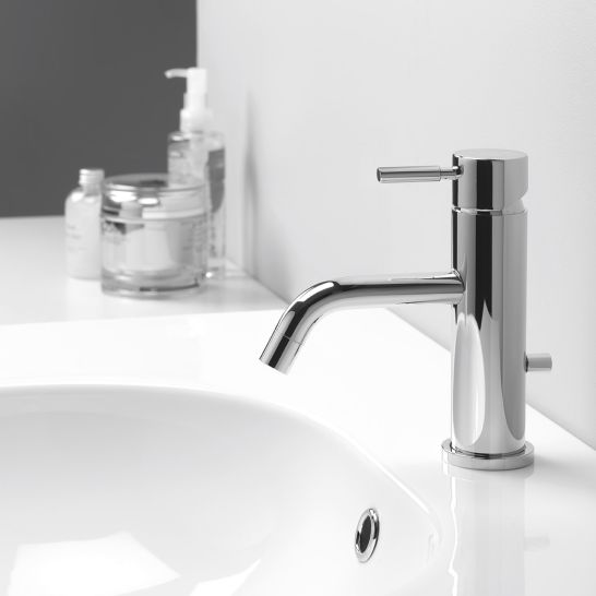Ein stilvolles Waschbecken mit einer zylindrischen Chromarmatur. Auf der Ablagefl&auml;che stehen diverse Pflegeprodukte. Zeitloses und elegantes Design.