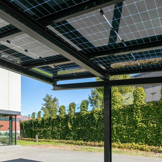 Modernes Carport mit Solarpanelen: Nachhaltige Energiegewinnung trifft stilvolle Architektur, erg&auml;nzt durch eine gr&uuml;ne, einladende Umgebung.