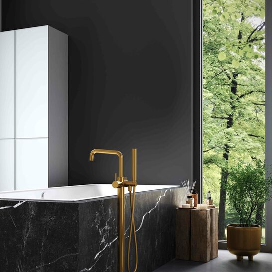 Luxuri&ouml;ses Badezimmer mit einer freistehenden Badewanne aus schwarzem Marmor und modernen goldenen Armaturen. Gro&szlig;e Fenster bieten einen Blick ins Gr&uuml;ne, erg&auml;nzt durch Pflanzen im Innenraum.