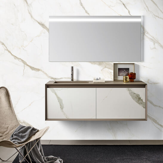 Moderner Waschtisch mit gro&szlig;em Spiegel und Marmorwand, daneben ein Stuhl mit Decke auf einem dunklen Teppich. Elegantes und minimalistisches Design.