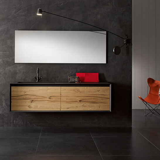 Modernes Badezimmer mit dunkler Wand, hängendem Holzschrank, großem Spiegel, stilvoller Beleuchtung, schwarzem Boden, orangefarbenem Stuhl und kleinem Tisch. Modernes Badezimmer mit dunkler Wand, hängendem Holzschrank, großem Spiegel, stilvoller Beleuchtung, schwarzem Boden, orangefarbenem Stuhl und kleinem Tisch.
