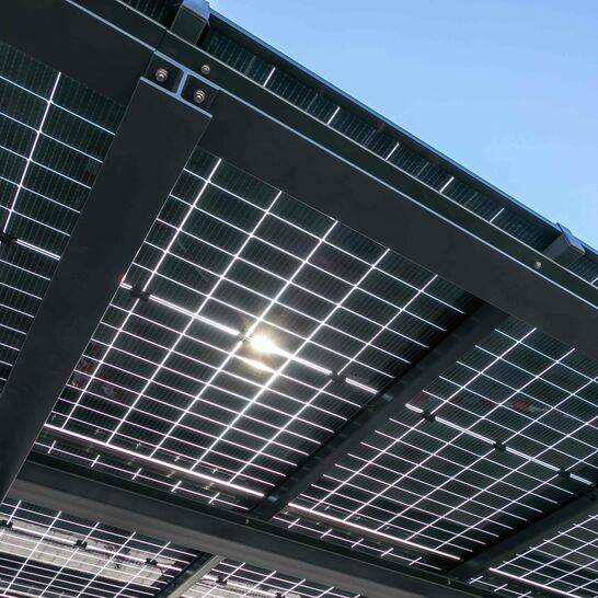 Ein Solardach mit mehreren Solarpaneelen, die in einem Metallrahmen angebracht sind. Die Sonne scheint durch die Paneele, und der Himmel ist klar und blau.