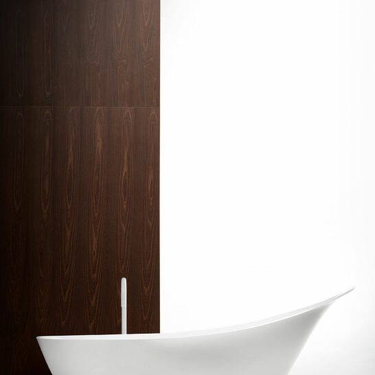 Ein modernes Badezimmer mit einer eleganten, weißen, freistehenden Badewanne. Die Wand im Hintergrund ist aus dunklem Holz, der Raum wirkt minimalistisch. Ein modernes Badezimmer mit einer eleganten, weißen, freistehenden Badewanne. Die Wand im Hintergrund ist aus dunklem Holz, der Raum wirkt minimalistisch.