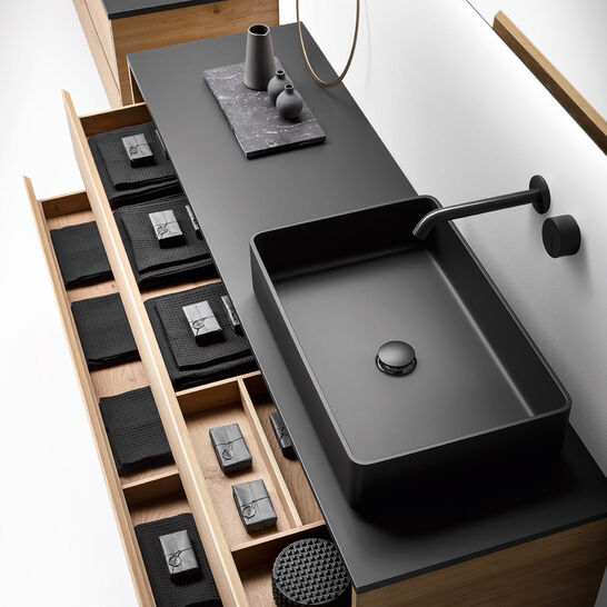 Modernes Badezimmerdesign mit schwarzem Waschbecken und passender Armatur. Holzschubladen zeigen geordnete Handtücher und Accessoires. Elegante Optik. Modernes Badezimmerdesign mit schwarzem Waschbecken und passender Armatur. Holzschubladen zeigen geordnete Handtücher und Accessoires. Elegante Optik.