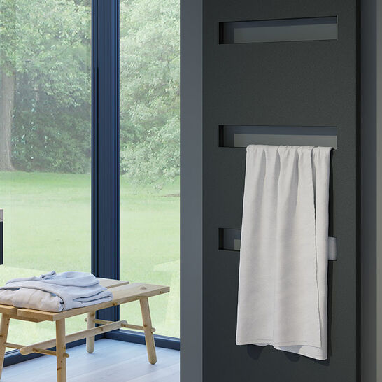 Schwarzer, moderner Heizkörper mit rechteckigen Öffnungen, daran hängt ein weißes Handtuch. Stilvoll und funktional in einem eleganten Raum. Schwarzer, moderner Heizkörper mit rechteckigen Öffnungen, daran hängt ein weißes Handtuch. Stilvoll und funktional in einem eleganten Raum.