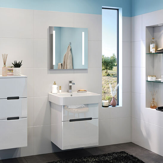 Helles Badezimmer mit weißen Fliesen, blauem Akzent, Waschbecken, Spiegel, hängenden Schränken und Fenster. Elegante Regale bieten zusätzlichen Stauraum
