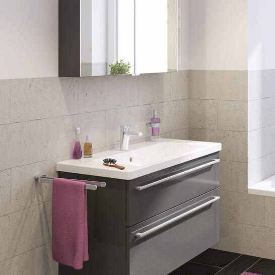 Modernes Bad mit beleuchtetem Spiegel, grauem Waschtisch, lila Handtuch, dunklen Fliesen. Heller, stilvoller Look mit schlichter Eleganz. Modernes Bad mit beleuchtetem Spiegel, grauem Waschtisch, lila Handtuch, dunklen Fliesen. Heller, stilvoller Look mit schlichter Eleganz.