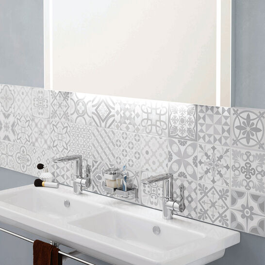 Modernes Badezimmer mit Doppelwaschbecken, stilvollen gemusterten Fliesen und beleuchtetem Spiegel. Helle und dekorative Einrichtungselemente. Modernes Badezimmer mit Doppelwaschbecken, stilvollen gemusterten Fliesen und beleuchtetem Spiegel. Helle und dekorative Einrichtungselemente.