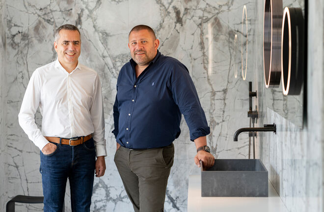 Zwei Männer stehen in einem stilvollen Raum mit Marmordekor. Einer trägt ein weißes Hemd, der andere ein blaues. Neben ihnen ist ein modernes Waschbecken. Zwei Männer stehen in einem stilvollen Raum mit Marmordekor. Einer trägt ein weißes Hemd, der andere ein blaues. Neben ihnen ist ein modernes Waschbecken.