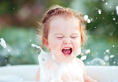 Ein lachendes Kleinkind spielt in einem Schaumbad, umgeben von Seifenblasen und Wasser. Es wirkt fröhlich und ausgelassen. Ein lachendes Kleinkind spielt in einem Schaumbad, umgeben von Seifenblasen und Wasser. Es wirkt fröhlich und ausgelassen.