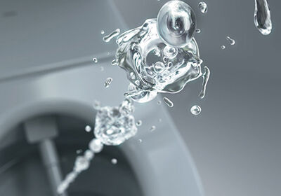 Nahaufnahme eines Wasserstrahls, der in eine Toilette spritzt. Die Wassertropfen sind eingefroren und klar sichtbar vor einem grauen Hintergrund. Nahaufnahme eines Wasserstrahls, der in eine Toilette spritzt. Die Wassertropfen sind eingefroren und klar sichtbar vor einem grauen Hintergrund.